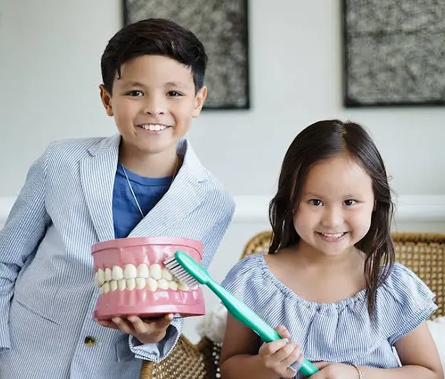 Kids smiling holding large tooth brush